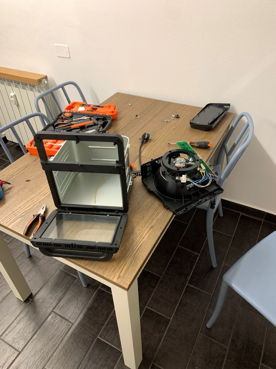 The oven fully taken apart on the kitchen table, with screws scattered around.